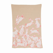 The Baby Rabbits Blanket by in2green is a beige eco throw adorned with a pattern of pink outlined rabbits and small flowers, ideal for gender-neutral decor.