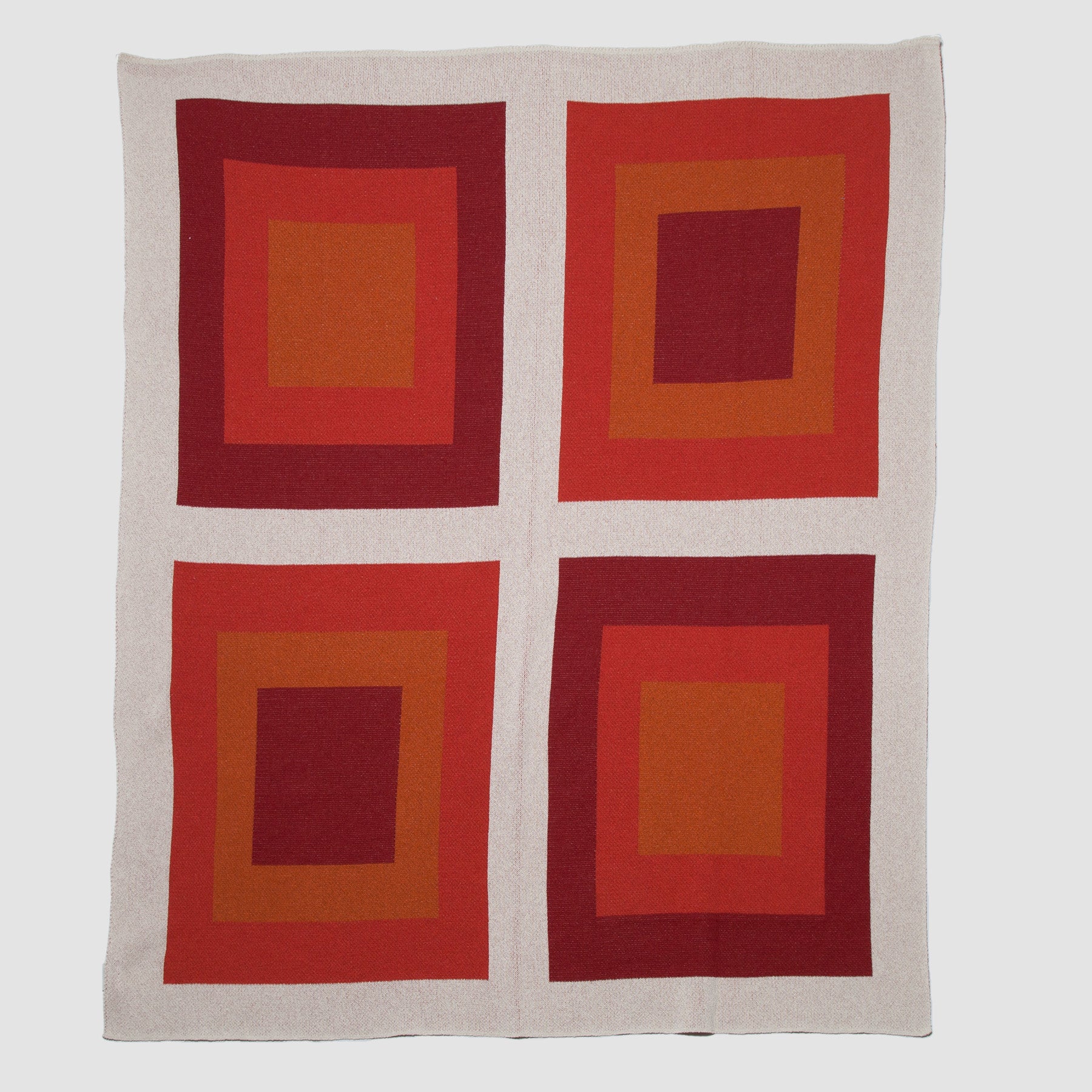 The Bauhaus Throw Blanket by in2green is beige with a 2x2 grid of iconic square designs in red and orange shades, blending Bauhaus-inspired style with an eco-friendly ethos for a sustainable home choice.