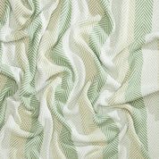 Introducing the Herringbone Hues Throw Blanket by In2Green, showcasing crumpled fabric with a herringbone pattern in alternating green and beige stripes. Made from recycled cotton in the USA, this eco-friendly throw blends sustainability with style.