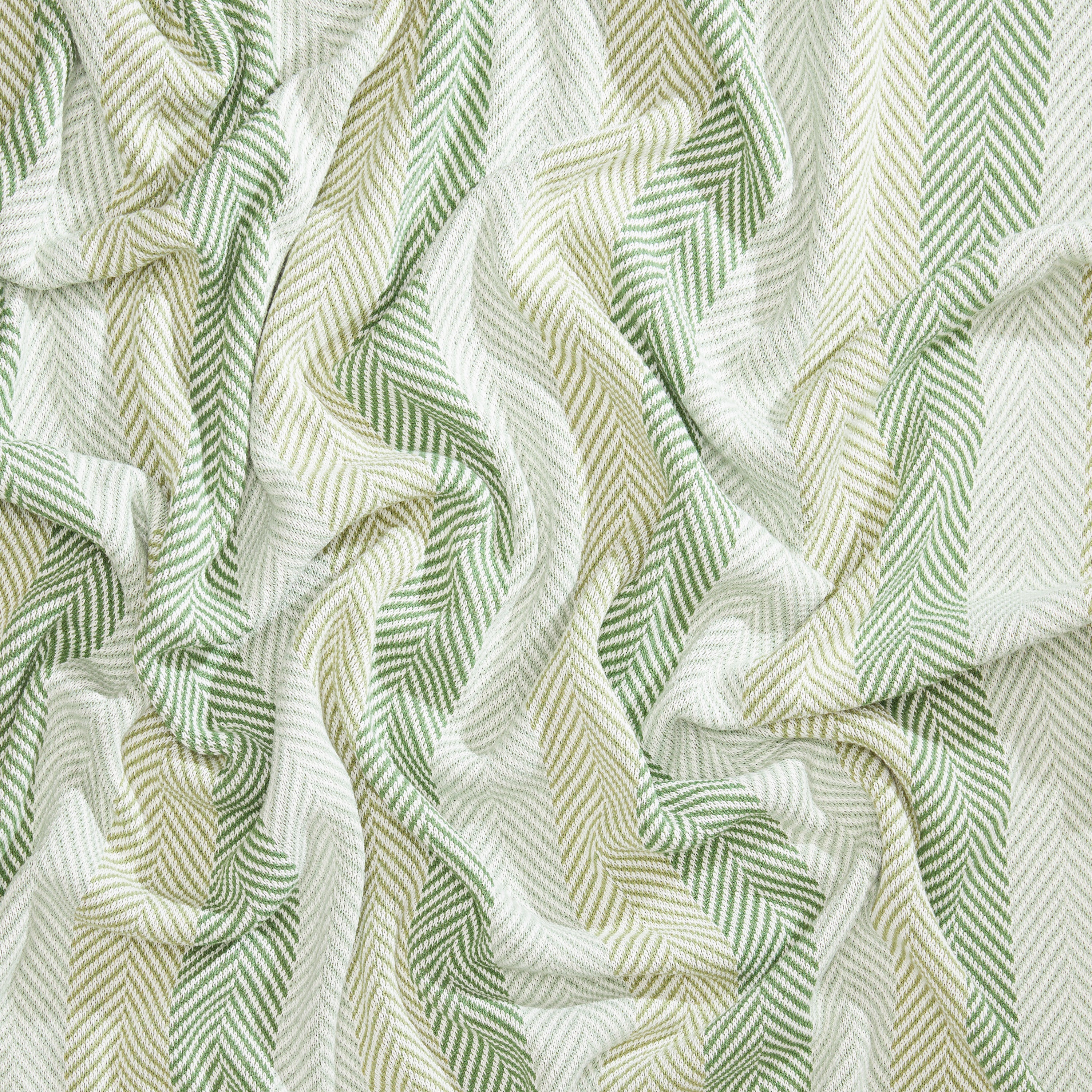 Introducing the Herringbone Hues Throw Blanket by In2Green, showcasing crumpled fabric with a herringbone pattern in alternating green and beige stripes. Made from recycled cotton in the USA, this eco-friendly throw blends sustainability with style.