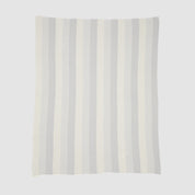 The Herringbone Hues Throw Blanket from In2Green, made in the USA with recycled cotton, features a rectangular design with alternating vertical stripes in light gray and off-white against a plain background.