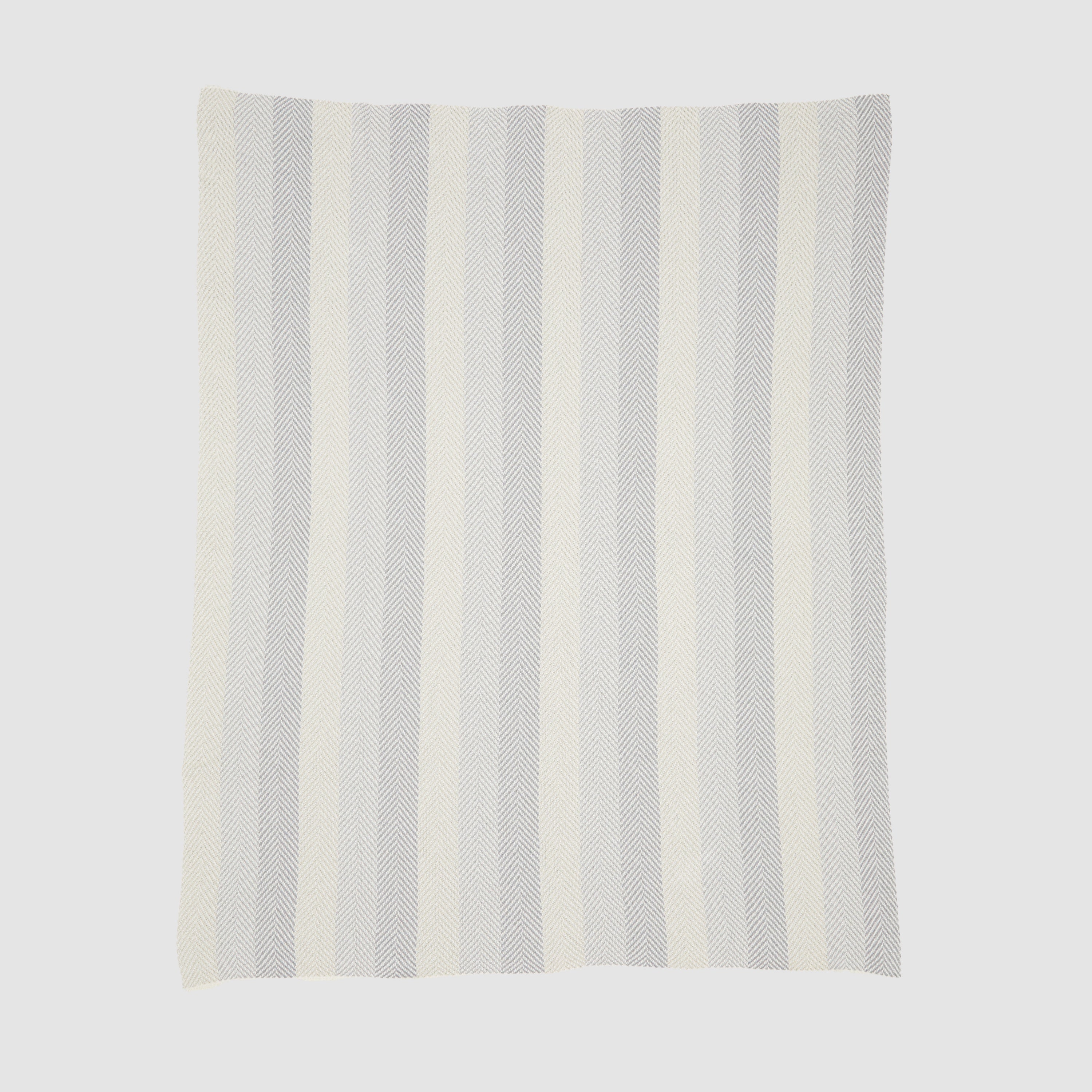 The Herringbone Hues Throw Blanket from In2Green, made in the USA with recycled cotton, features a rectangular design with alternating vertical stripes in light gray and off-white against a plain background.