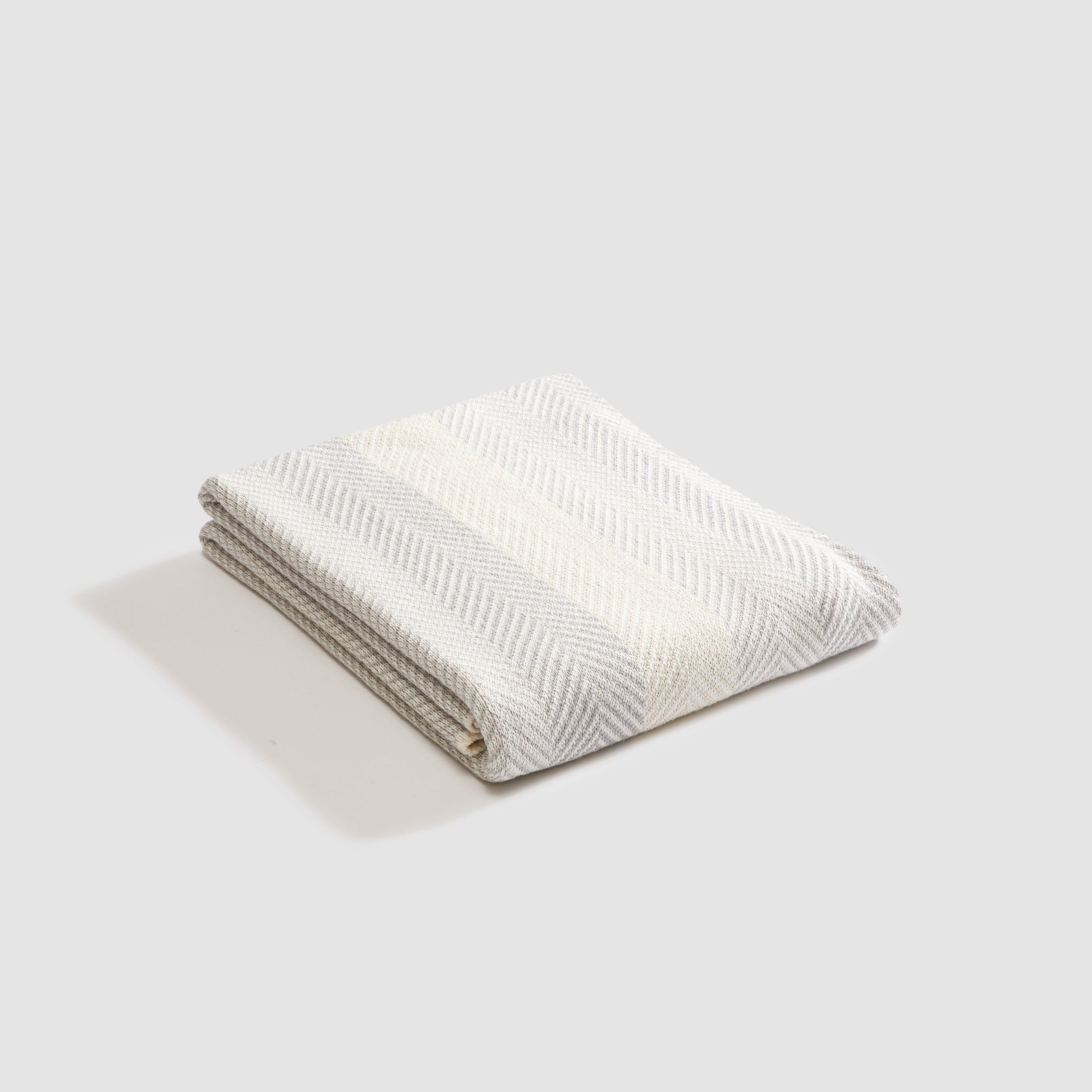 The Herringbone Hues Throw Blanket by In2Green, made in the USA from recycled cotton, seamlessly combines style and sustainability with its folded striped design on a herringbone-patterned background.