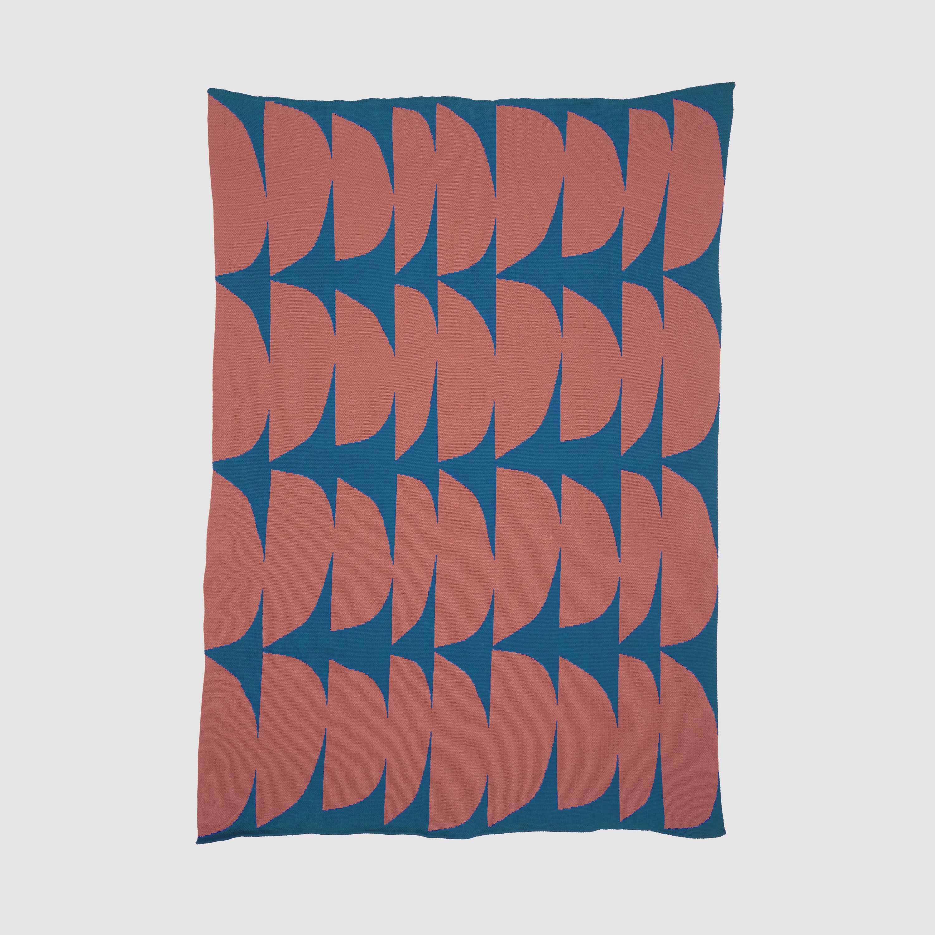 The Poly Kaareva Throw Blanket by Petra Kaksonen from in2green's outdoor collection features a geometric pattern of interlocking red and blue shapes on a white background, crafted from recycled polyester.