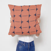 A person holds the Poly Kaarna Pillow by Petra Kaksonen, showcasing a stunning geometric Nordic design. The pillow features blue and rust circles on white, crafted from recycled polyester by in2green, blending sustainability with style.