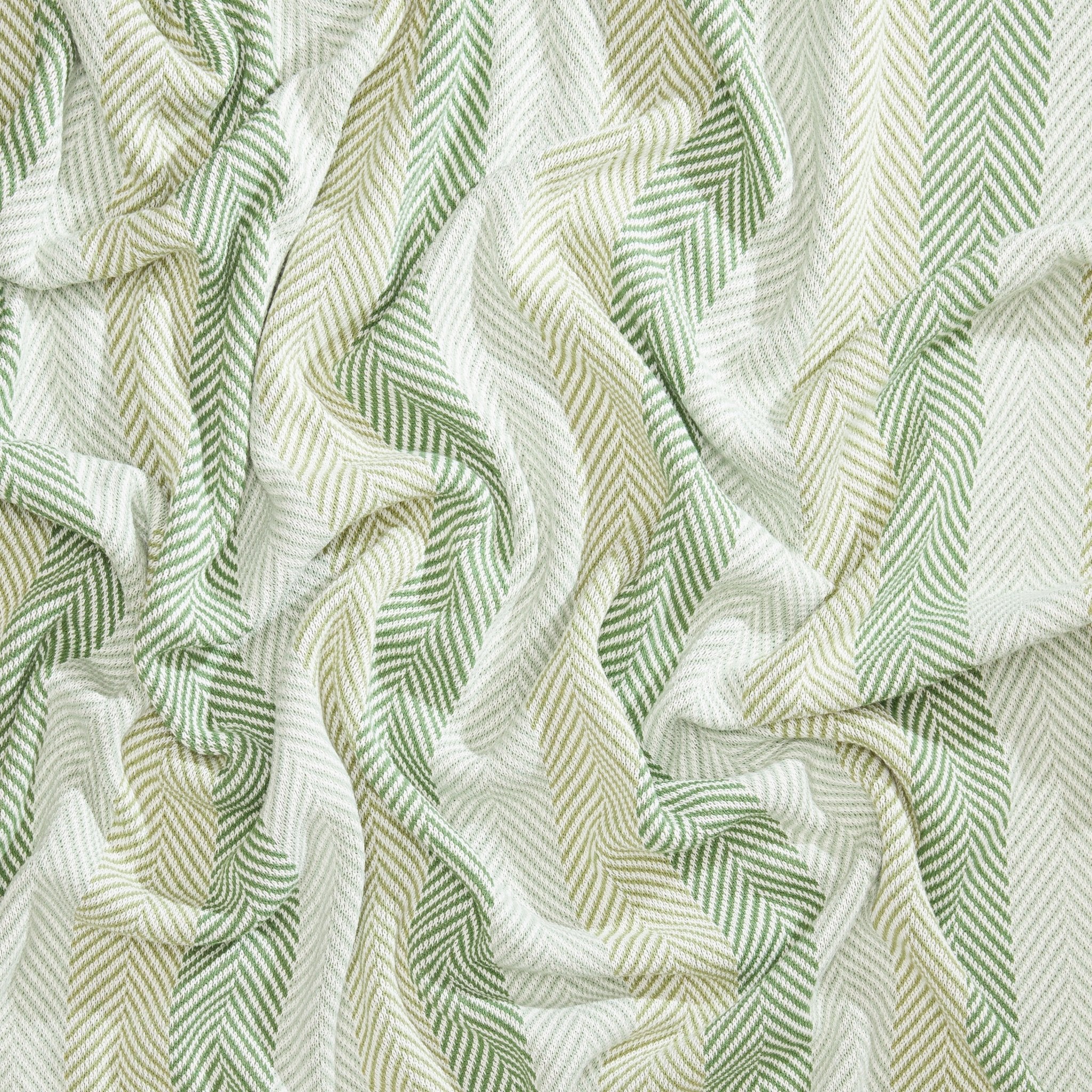 Introducing the Herringbone Hues Throw Blanket by In2Green, showcasing crumpled fabric with a herringbone pattern in alternating green and beige stripes. Made from recycled cotton in the USA, this eco-friendly throw blends sustainability with style.