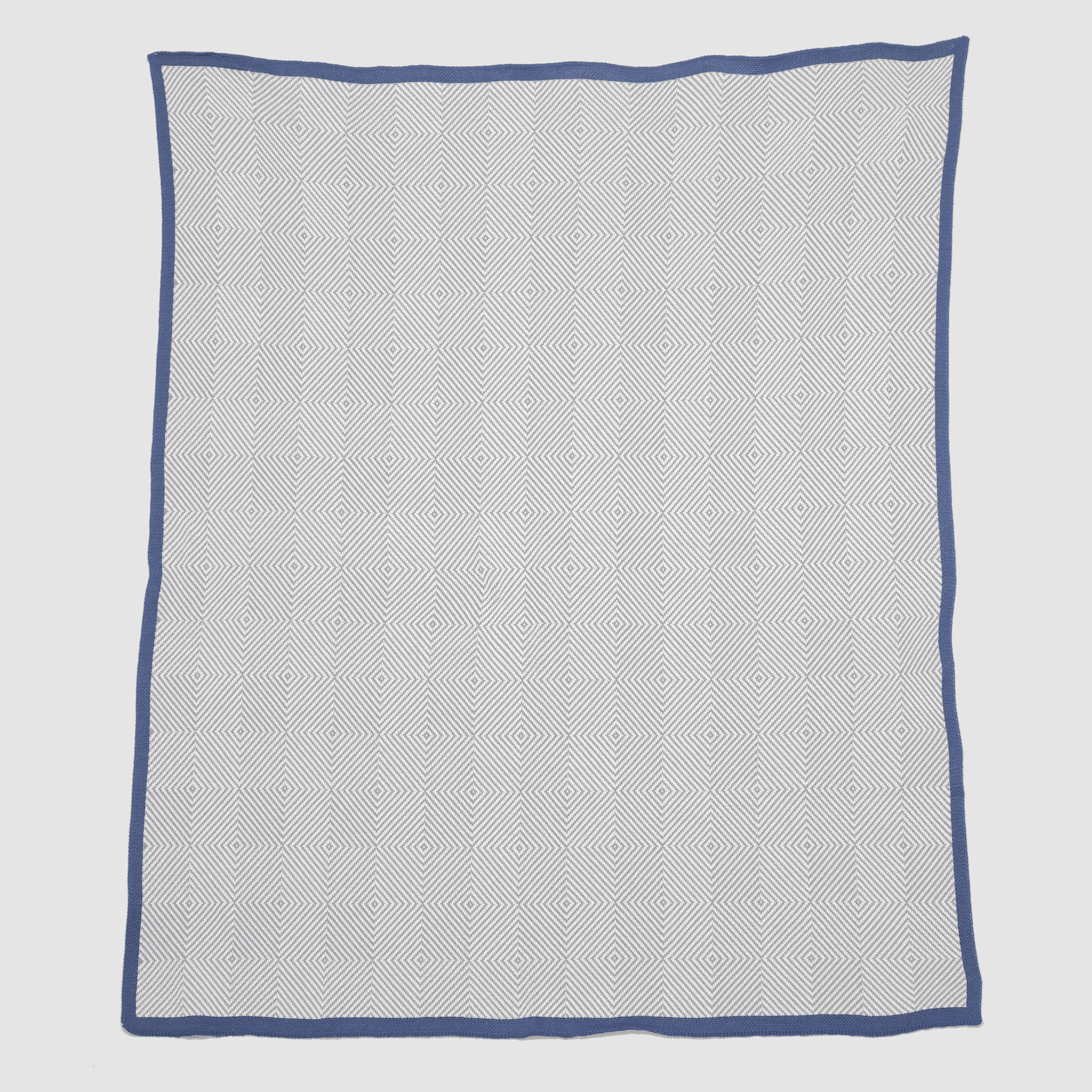 The in2green Poly Woven Square Throw Blanket is a white square blanket featuring a blue border and repeating diamond pattern, made from 100% recycled polyester.